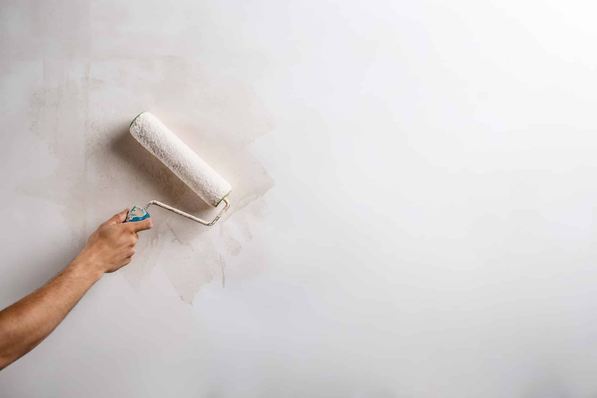 Detailný záber na ruku, ktorá drží valček a maľuje stenu na bielo.